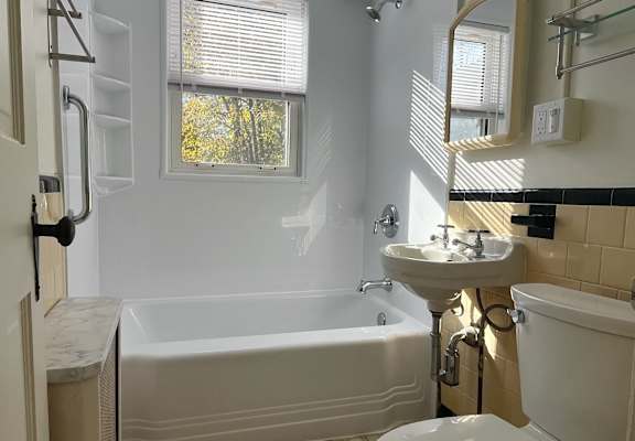 A white toilet is in a bathroom with a white tub and sink.