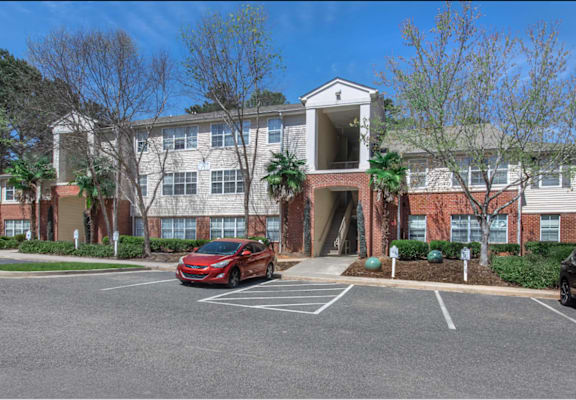 A red car is parked in a parking lot in front of a building.