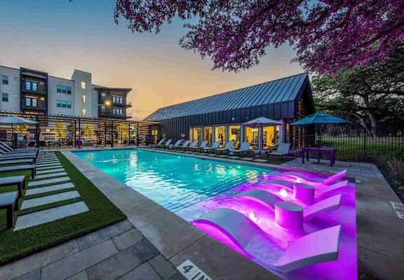 an outdoor pool with lounge chairs and a spa at night