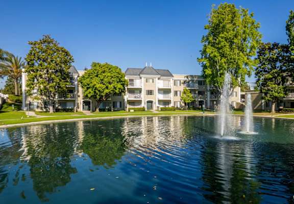 A fountain in the middle of a lake with a building in the background.