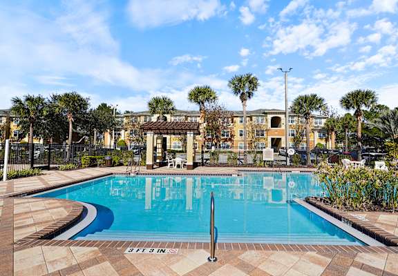 A pool surrounded by a brick patio and palm trees.