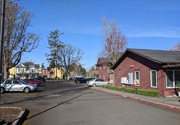 A street view with cars parked on the side of the road and a red building in the background.