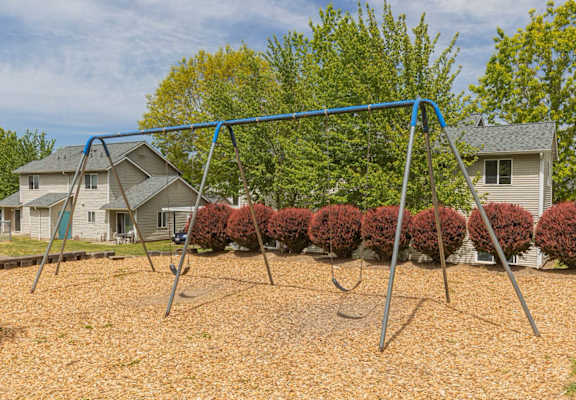A swing set in a backyard with a house and trees in the background.