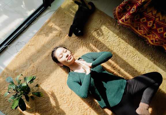 Young woman with cat meditating on carpet
