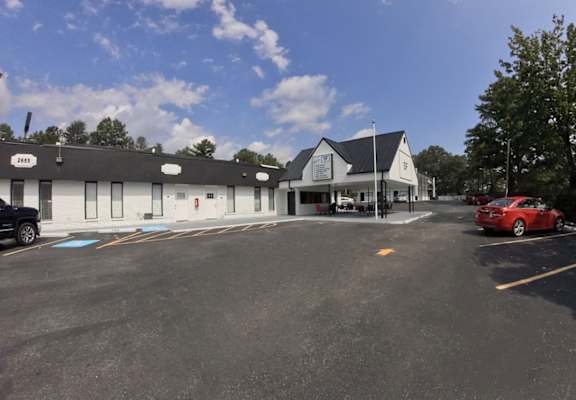 a parking lot in front of a white building with a black roof