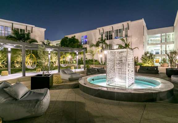 a fountain in the middle of a courtyard with seating and a pool at night