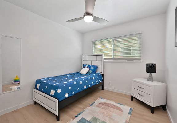A bedroom with a bed, nightstand, and a rug on the floor.
