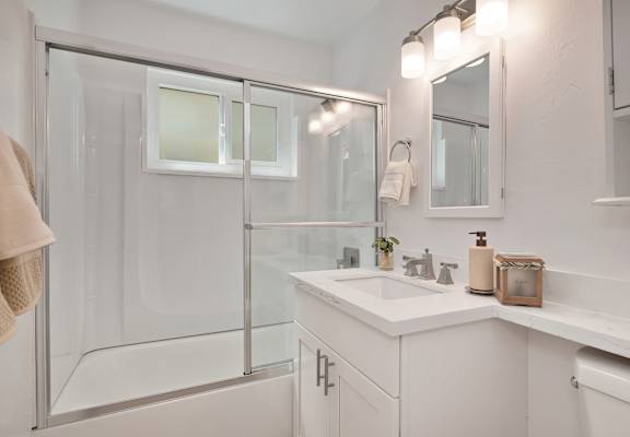 A white bathroom with a glass shower door and a white sink.