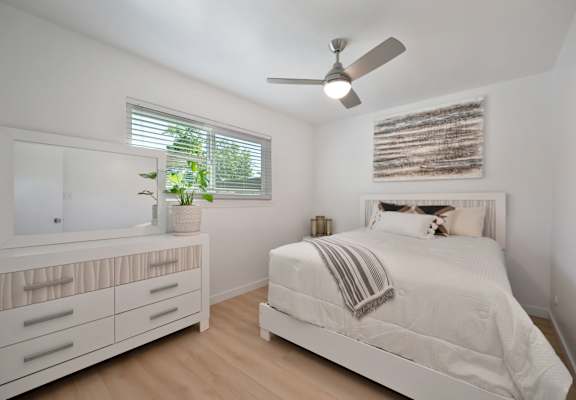 A white bedroom with a bed, dresser, and mirror.