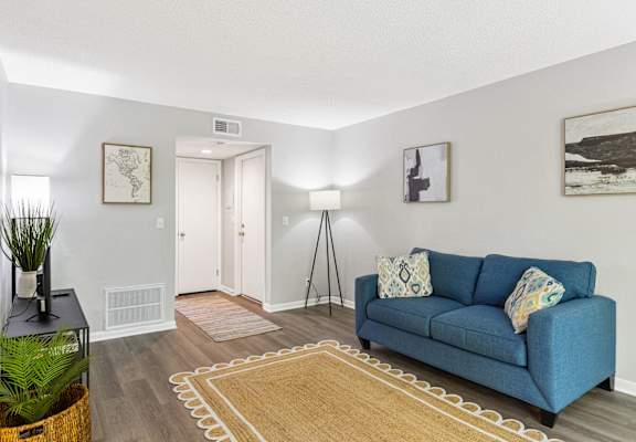 A blue couch with a white pillow is in the middle of a room with a rug on the floor.
