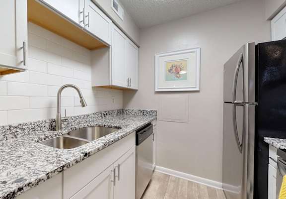 A kitchen with a black fridge and a sink with a marble counter top.