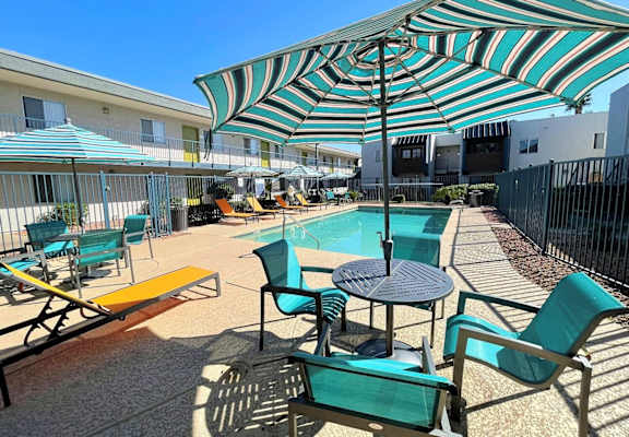 A sunny day at the pool with a striped umbrella providing shade.