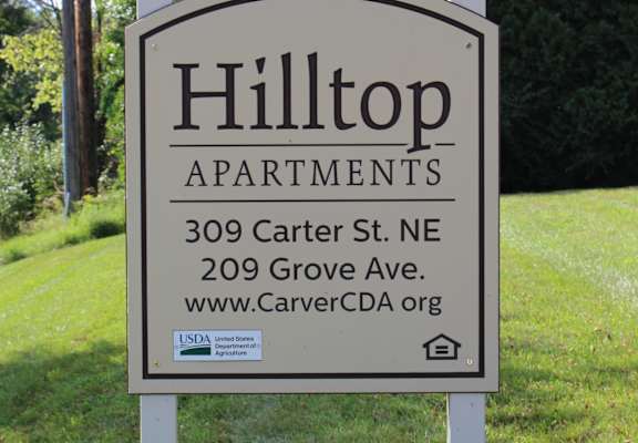 A sign for Hilltop Apartments is displayed in front of a green lawn.