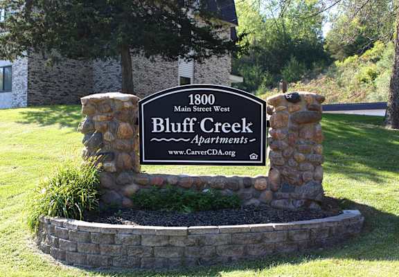 A sign for Bluff Creek Apartments is displayed in front of a building.