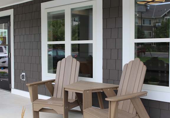 Two chairs and a table are on a porch.