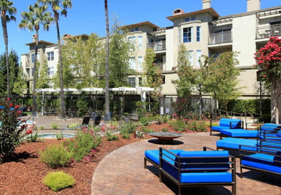 an outdoor lounge area with blue lounge chairs and a fire pit in front of an apartment building