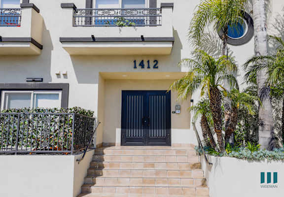 a house with a black door and a staircase with a palm tree in front of it