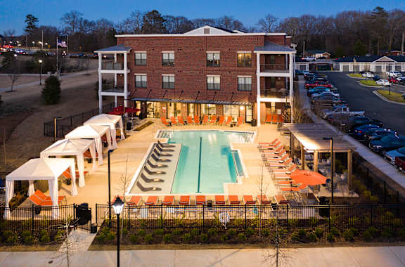 an aerial view of a resort style swimming pool with orange lounge chairs and white umbrellas at The Flats at Southlawn Apartments, Georgia