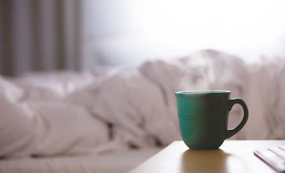 A mug with steam coming out of in front of bed with white linens