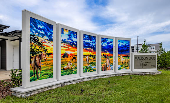 A row of four large paintings of horses in a field with the text "MADISON OAKS" on the right.