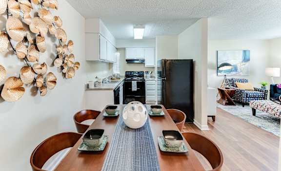 a dining area with a wooden table and chairs and a kitchen in the background