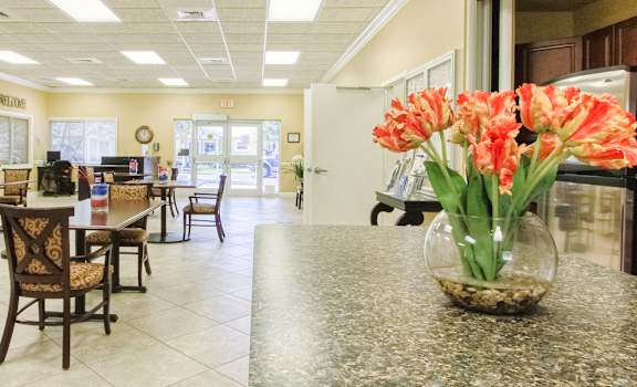 Community room with tables, chairs, and kitchen with flowers on island