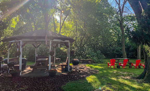 A gazebo is surrounded by red chairs and is in a lush green garden.
