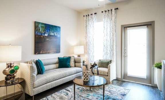 A living room with a couch, a painting, a fan, and a chair.