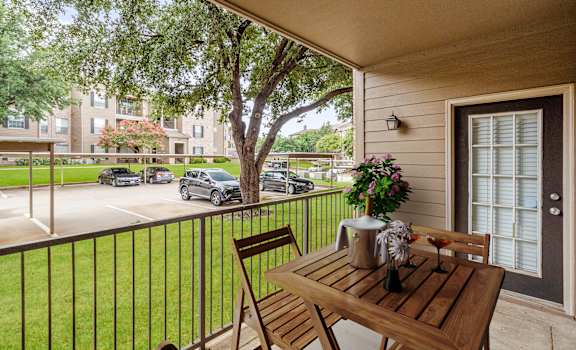 a patio with a wooden table and chairs on a balcony at The Clairborne Apartment Homes, Grand Prairie, TX, 75050