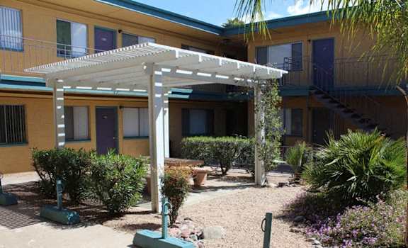 a courtyard with a white pergola in front of a yellow building