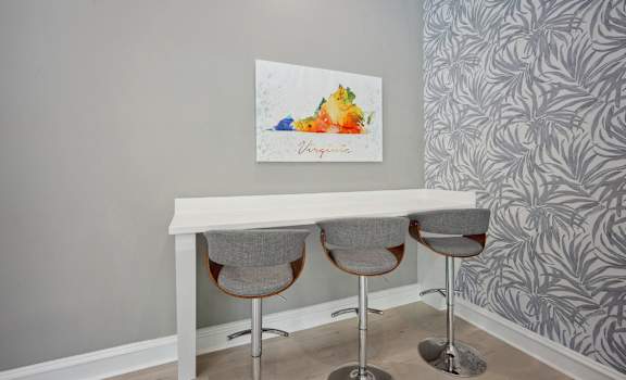 a white desk with three chairs in a room with a blue wall and a painting