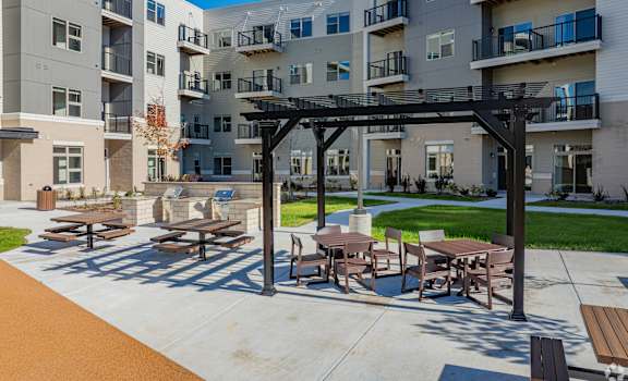A patio with tables and chairs is in front of apartment buildings.