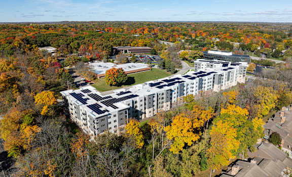 A large white building with a green roof surrounded by trees with orange and yellow leaves.