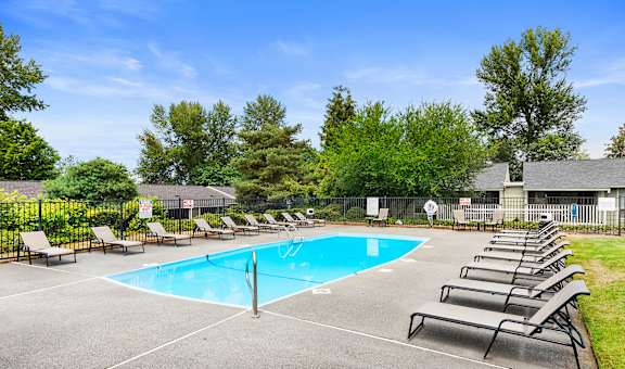 our resort style swimming pool is surrounded by lounge chairs and trees