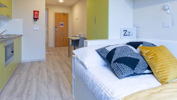 a bedroom with a bed and a kitchen in the background