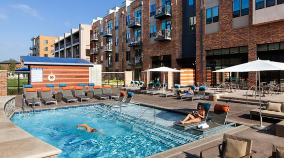 an outdoor pool with lounge chairs and umbrellas in front of a brick building