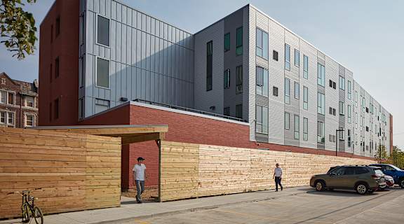A modern building with a red and grey facade and a wooden fence in front.