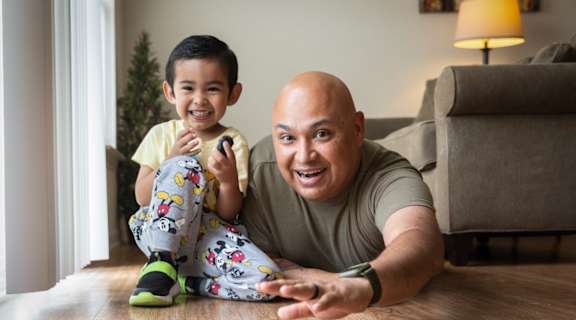 A man and a boy are playing with a small toy car on the floor.