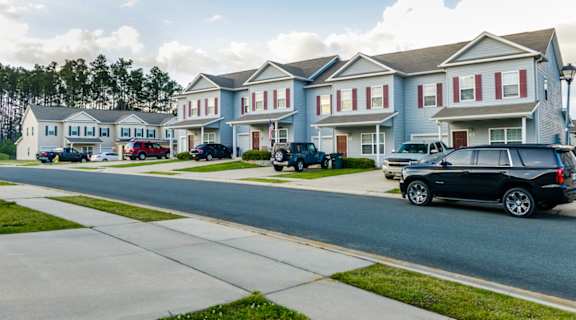 A black SUV is parked on the side of a street in front of a row of houses.