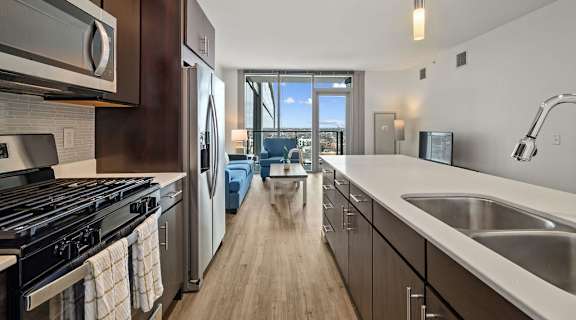 a kitchen with wooden cabinets and stainless steel appliances and a view of the living room at Halsted Flats Apartments, Chicago, IL, 60613