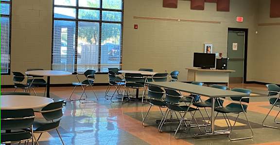 A room with tables and chairs and a TV on a stand.