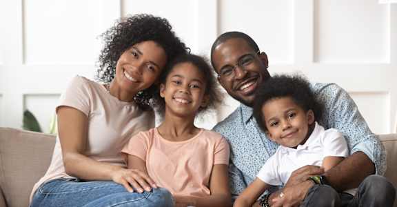 A family of four is sitting closely together on a couch.