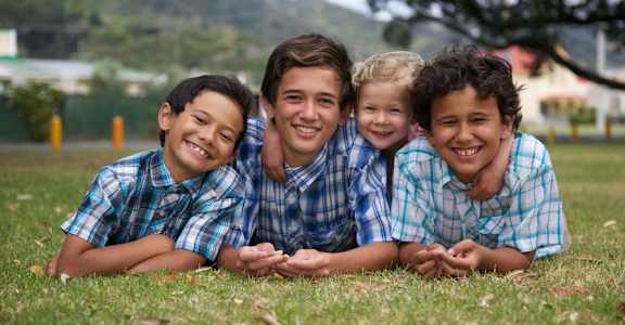 Four children wearing plaid shirts are lying on the grass.