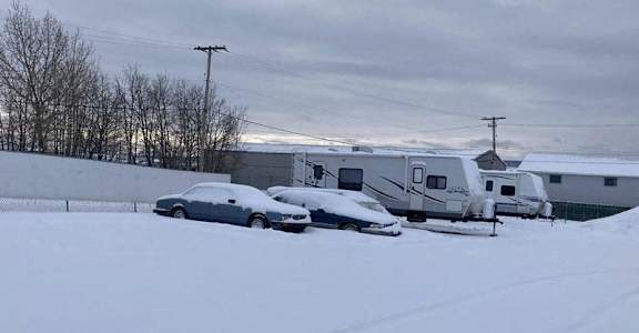 A car is parked in the snow next to a trailer.