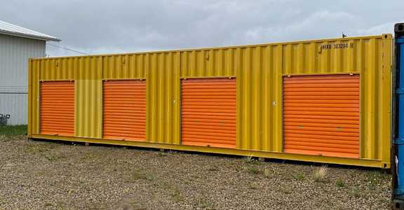 A yellow container with orange doors is parked in a gravel lot.