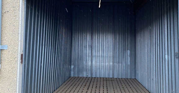 The image shows the interior of a storage unit with a wooden floor and metal walls.