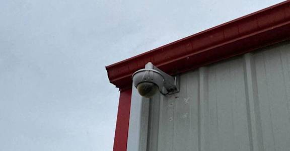 A grey building with a red trim and a security camera mounted on it.