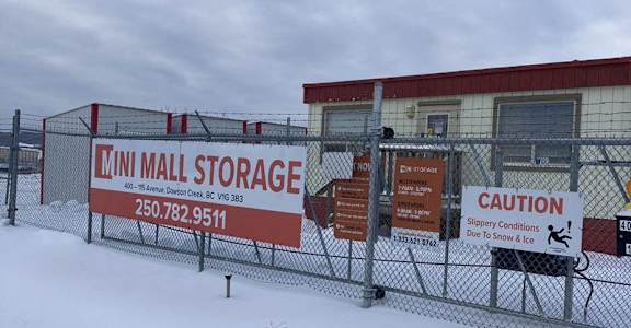 A storage facility is covered in snow and has a caution sign for slippery conditions.
