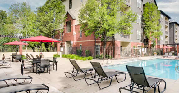 A pool surrounded by chairs and umbrellas in a courtyard.