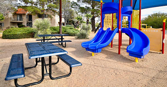 A playground with a blue slide and a picnic table.